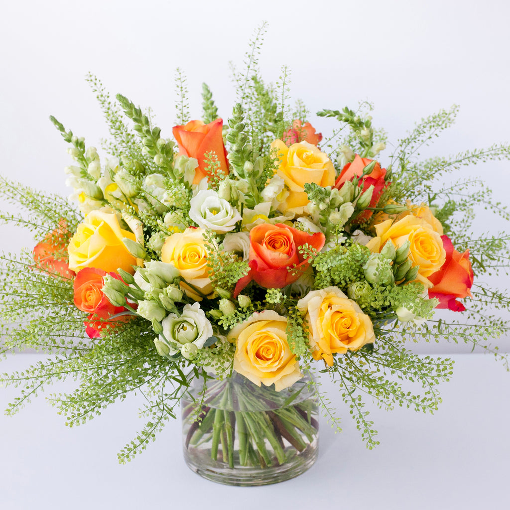 Image of yellow roses, white antirrhinum, green lisianthus, orange roses and foliage in a vase 