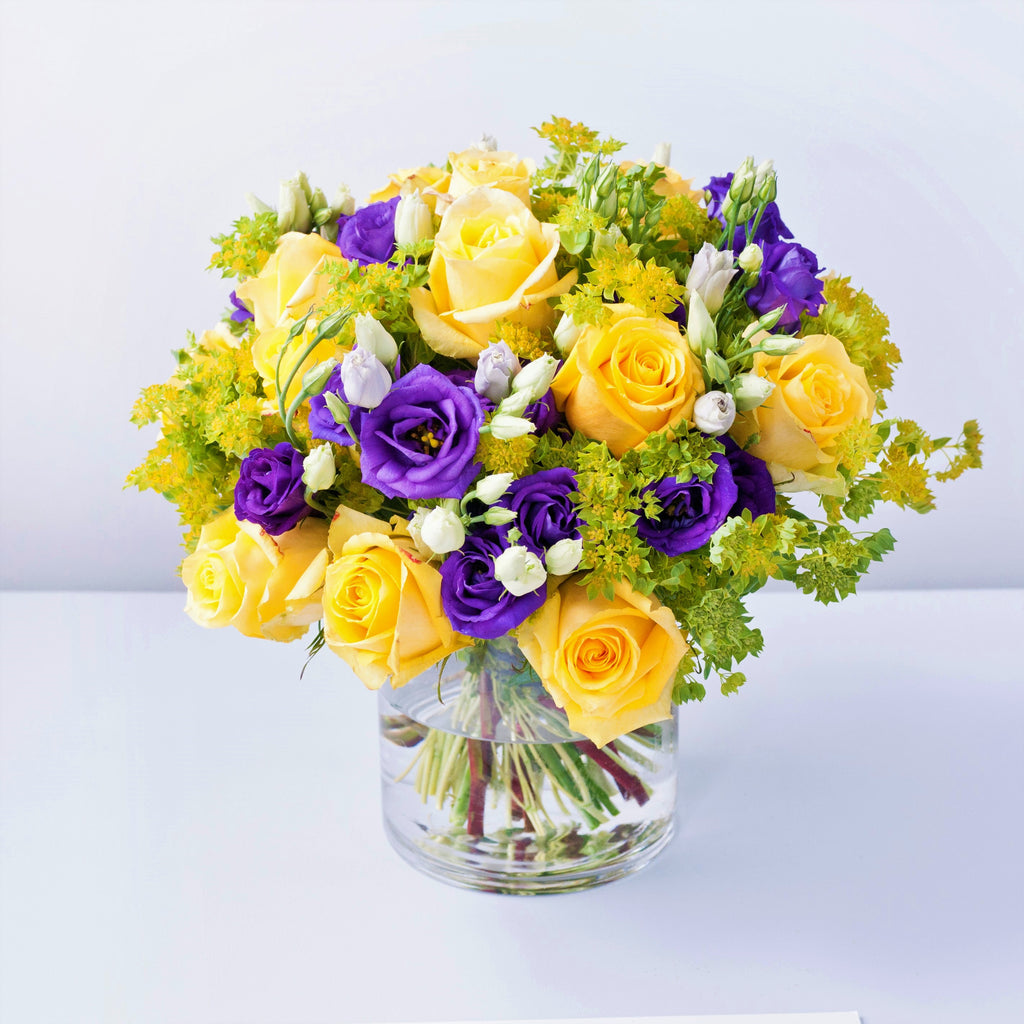 Yellow roses, purple lisianthus and foliage in a vase