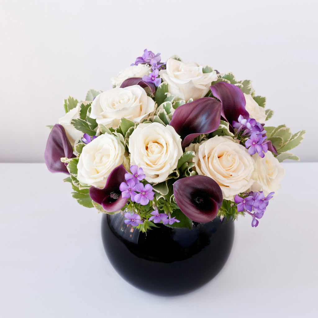 Image of white roses, burgundy calla lilies, purple phlox and foliage in a black goldfish bowl vase - Sherree Francis Flowers 