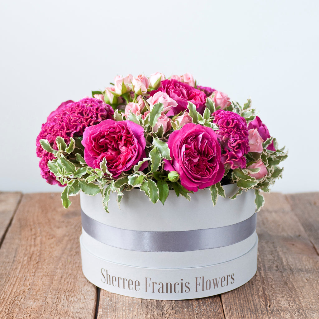 Image of hat box filled with cerise pink piano rises, pink celosia, pink spray roses and foliage 