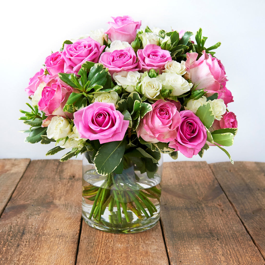 Vase of bubble gum pink roses and white spray roses and foliage.